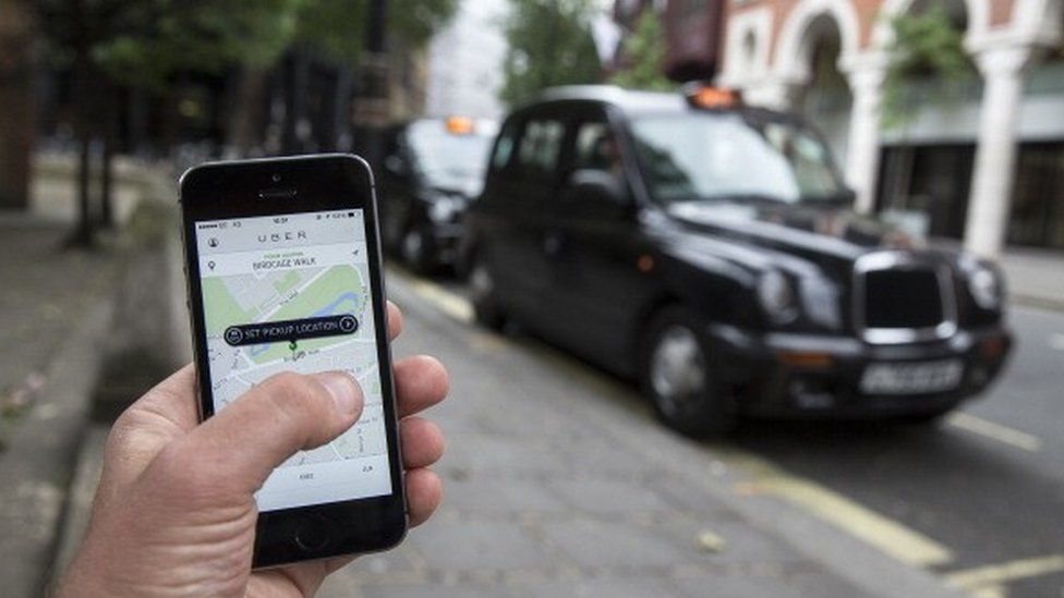 The Uber app on a smarphone with a black cab in the background