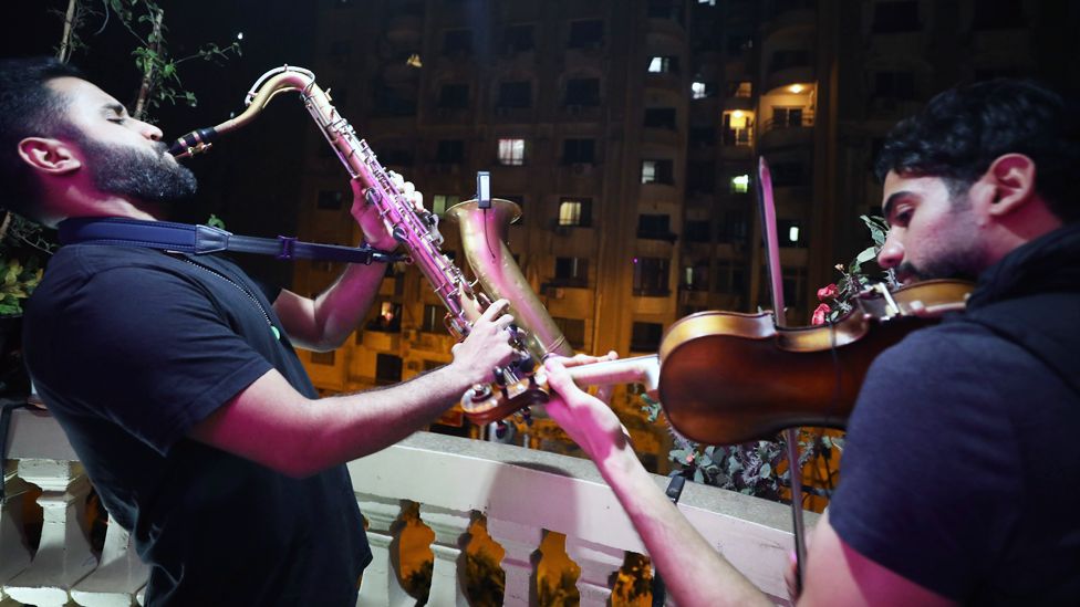 Mahmoud Saad (L) plays saxophone and Mohamed Adel (R) violin on their balcony during curfew in Giza, Egypt - Wednesday 1 April 2020