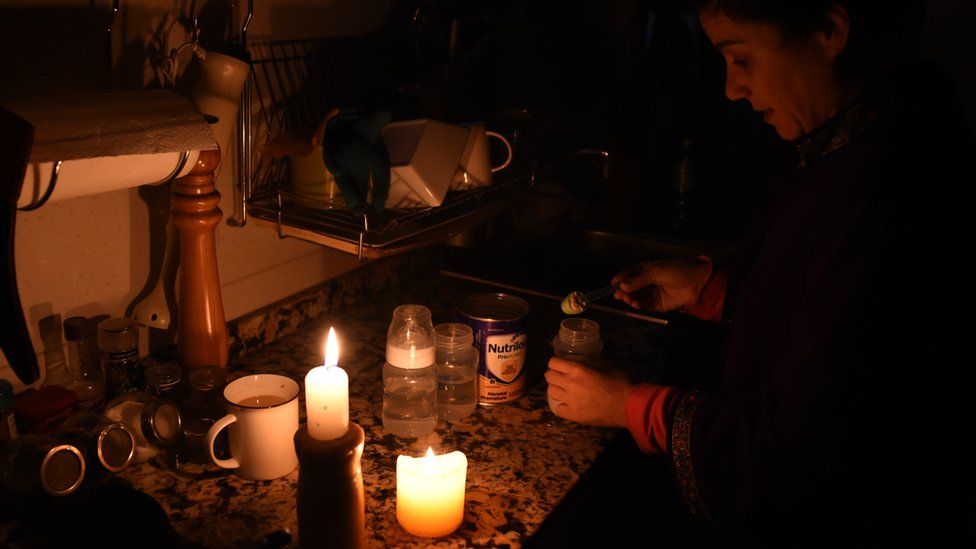 A woman prepares milk bottles using candles at her home in Montevideo on June 16, 2019 during a power cut