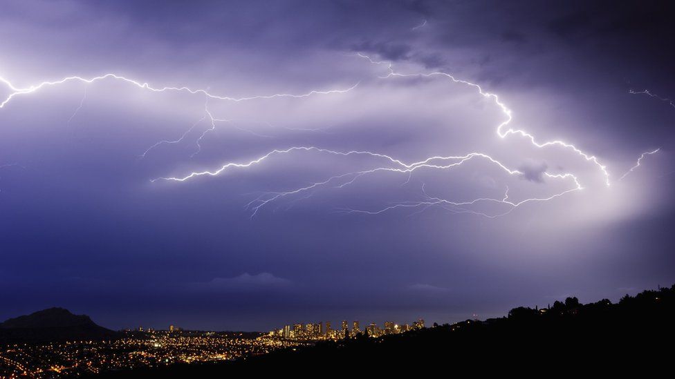 Lightning bolts over a city in a valley at night