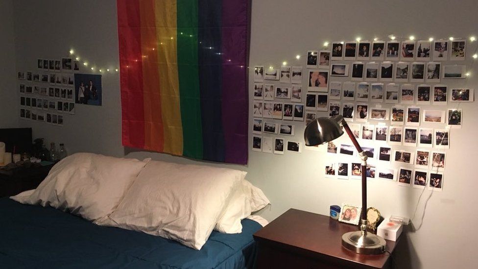 A rainbow flag with a selection of photographs either side of the wall