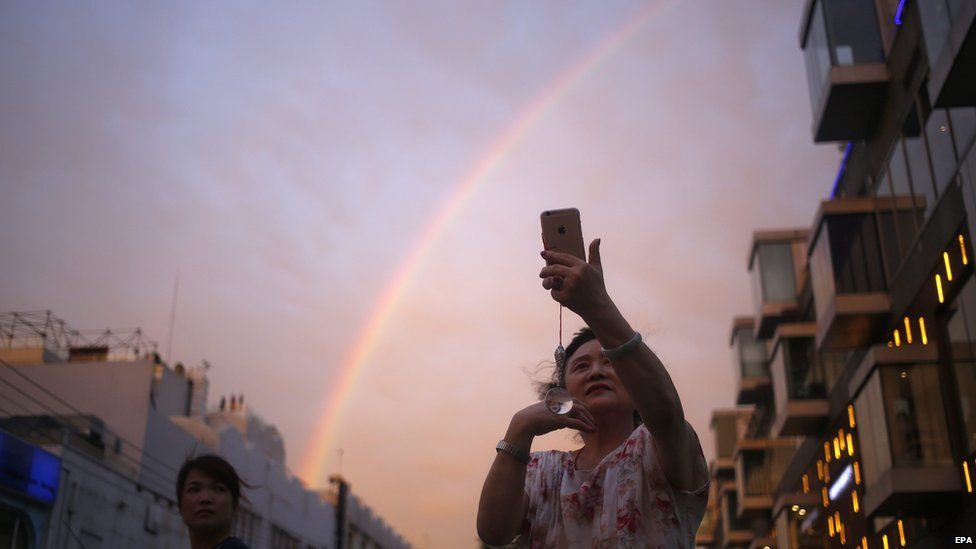 A Chinese woman takes a selfie with her mobile phone in front of a rainbow in Beijing, China on 3 August 2015