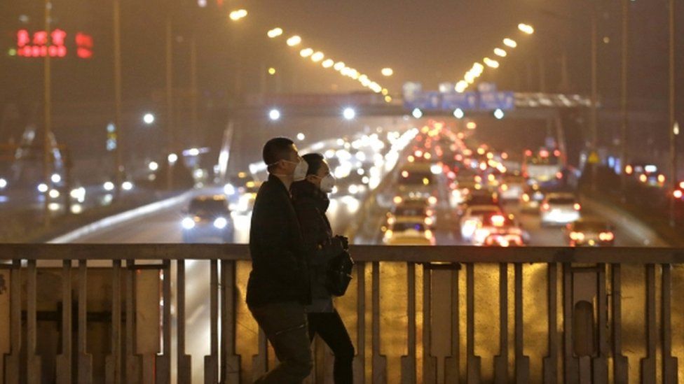 People wearing protective masks on an overpass during the evening rush hour amid the heavy smog in Beijing, 7 Dec