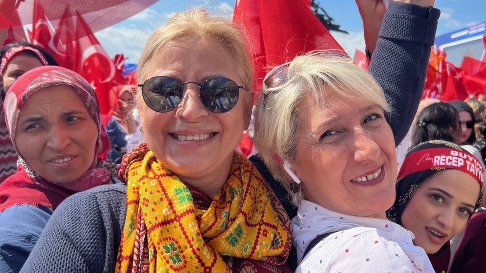 Secular women flanked by women in headscarves smile for the camera.