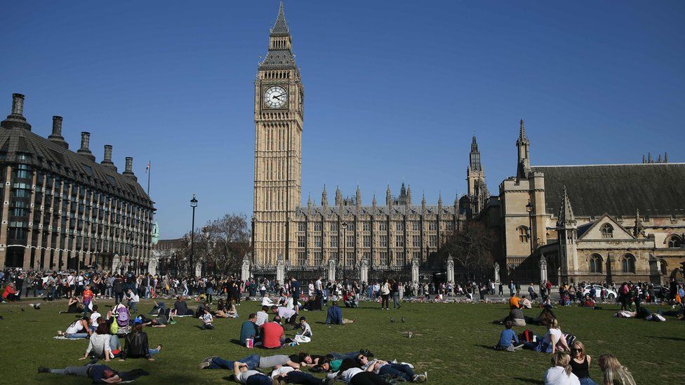 People relax in the sunshine in Parliament Square in front of the Houses of Parliament in central London