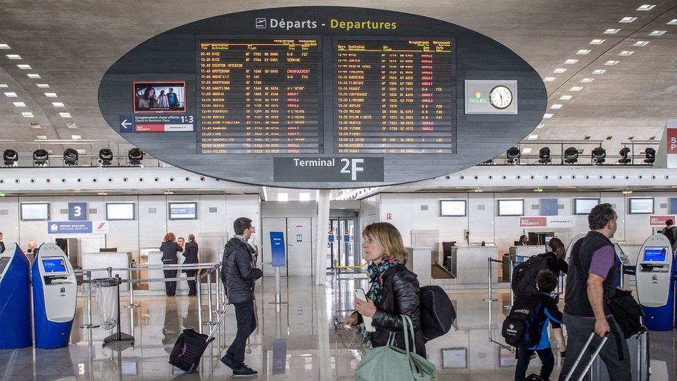 passengers walking past a departures board where many flights are listed as cancelled
