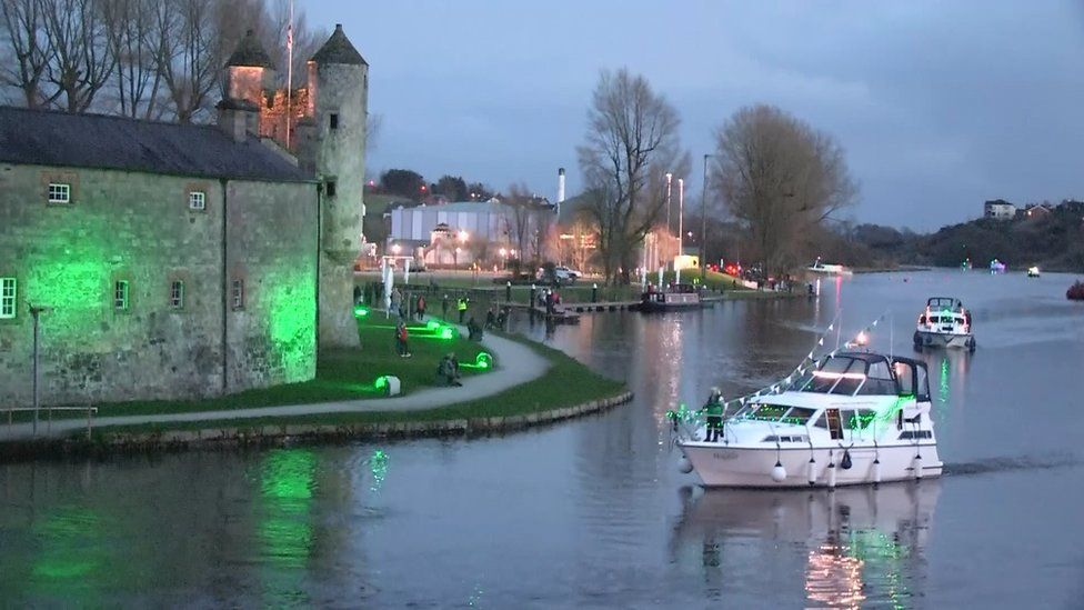 Boats on the River Erne lit up in green with Enniskillen Castle in the background