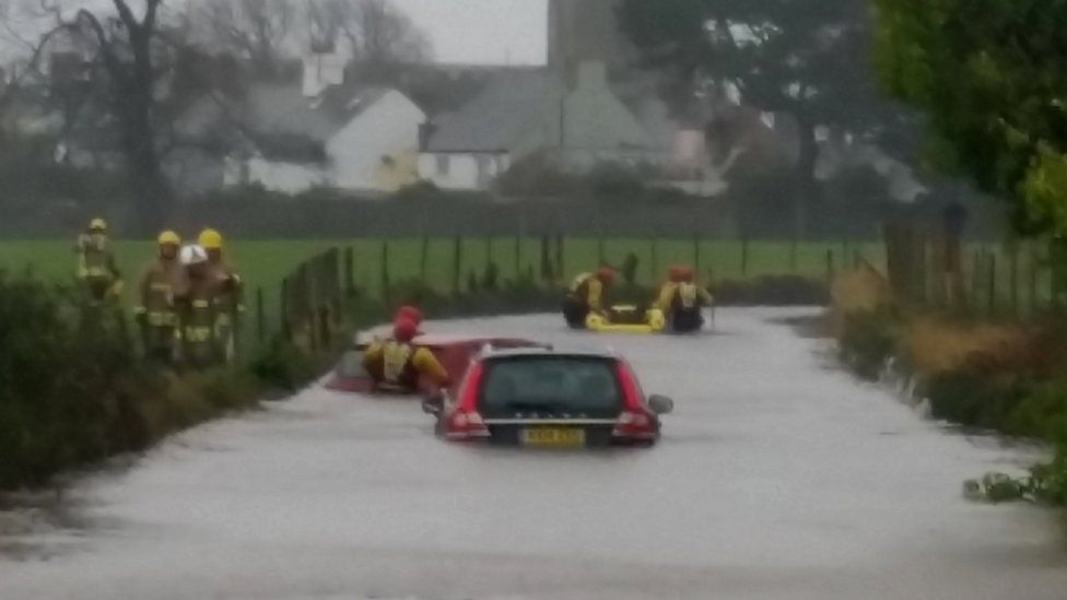 Firefighters rescue a woman from a car stuck in floods in Beaumaris, on Anglesey