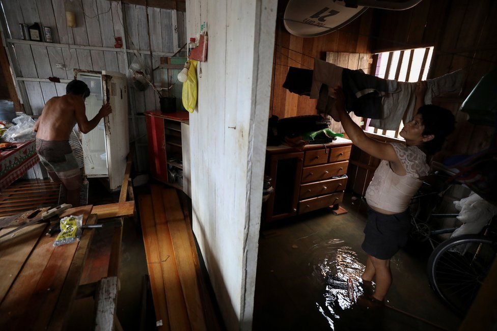 Manoel de Oliveira Cardoso and his wife Eliana dos Santos Madi clean up their flooded house by the rising Solimoes river