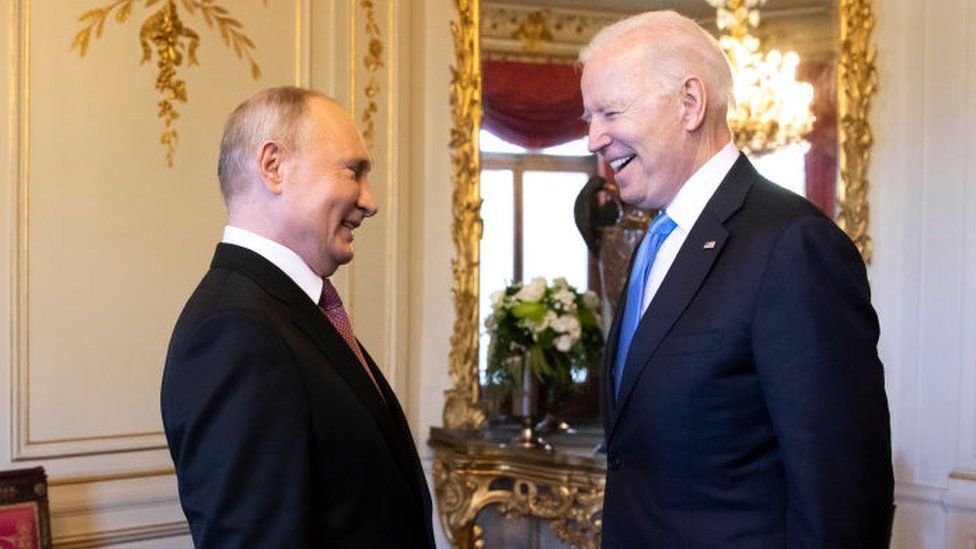 Putin and Biden laugh together in a luxuriously decorated room