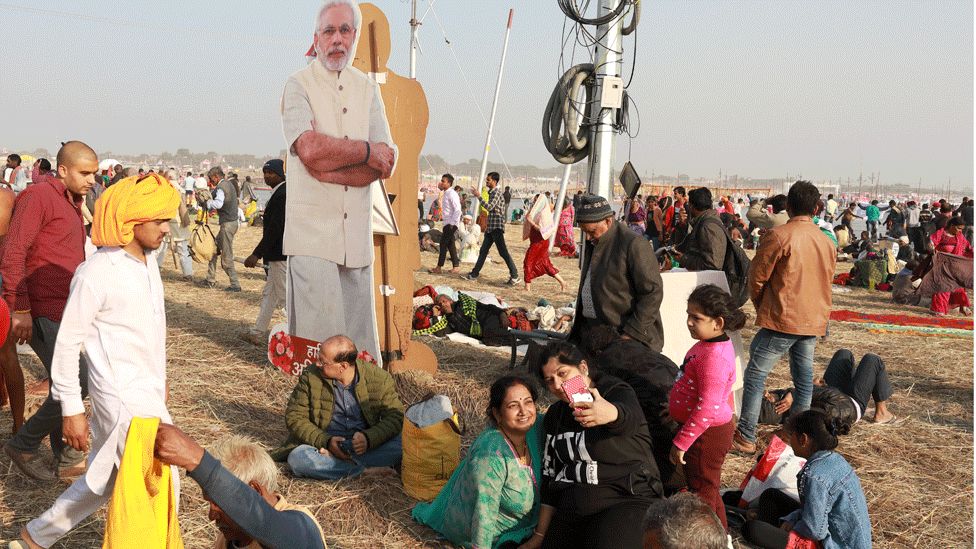 People sit near a cardboard cut-out of Narendra Modi