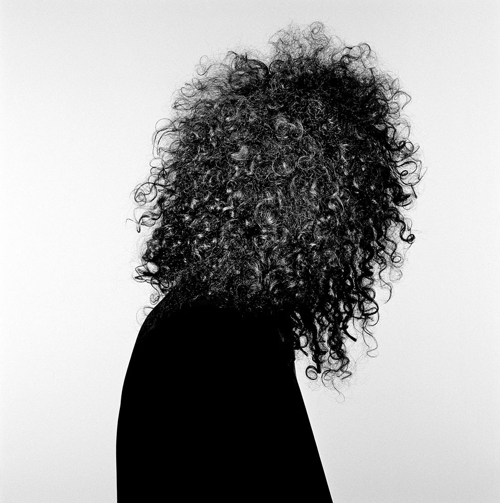 A black and white portrait of guitarist Brian May showing his hair
