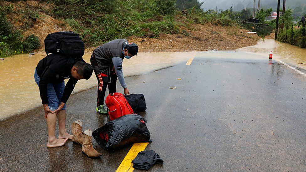 Men prepare to cross a mudslide blocking a road after the passage of Storm Eta