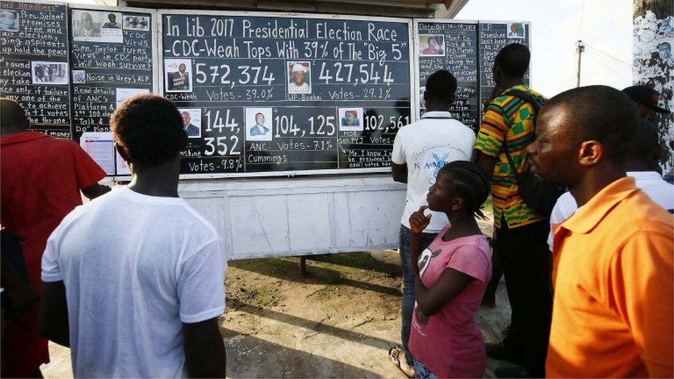Liberians read from a 'Daily Talk' chalkboard by a roadside in Monrovia, Liberia. 17th October 2017. Liberians who can not afford to buy a newspaper, get information from a public chalkboard and the results of the just ended Presidential and General elections.