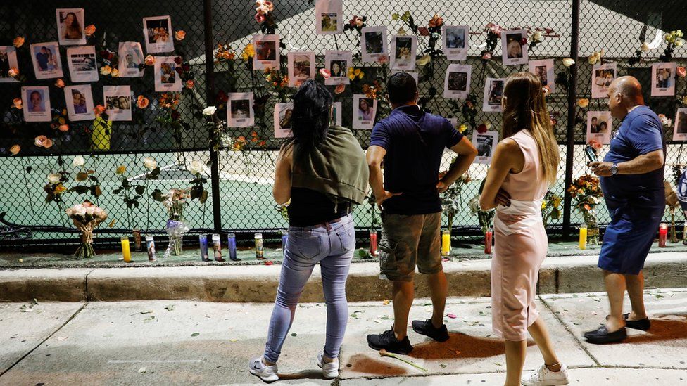 People look at flowers and pictures of missing people hanging on a fence at the memorial for victims of a partially collapsed residential building as the emergency crews continue search and rescue operations for survivors, in Surfside, near Miami Beach, Florida, U.S. June 25, 2021.