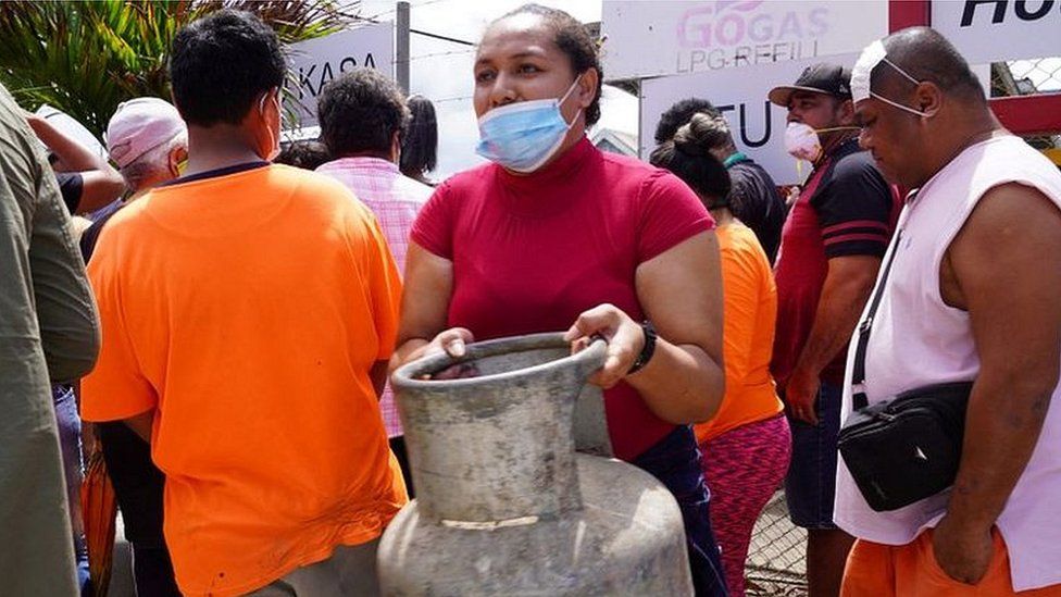 A woman (C) carries a refilled gas container in the centre of the capital Nuku'alofa ahead of the country's first lockdown on February 2, 2022, after Covid-19 was detected in the previously virus-free Pacific kingdom as it struggles to recover from the deadly January 15 volcanic eruption and tsunami.