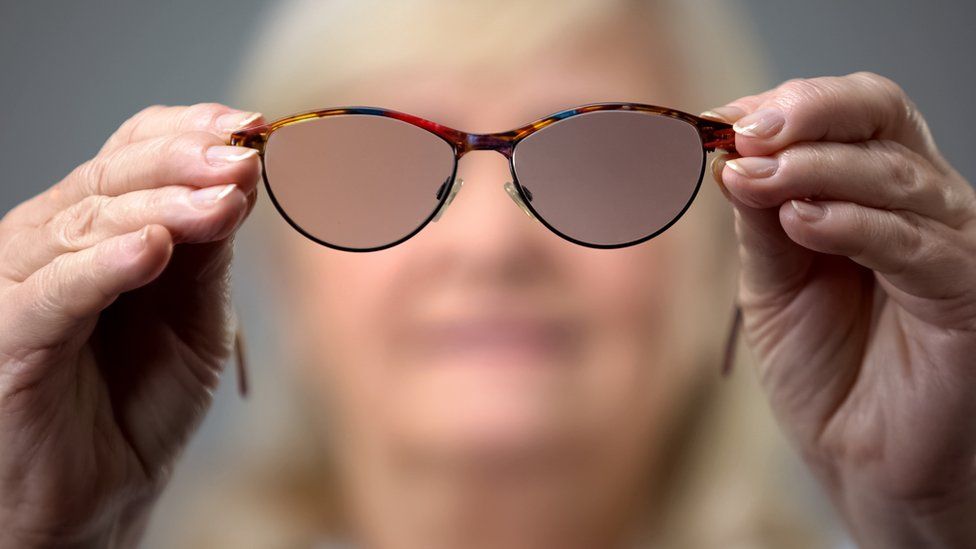 Blurred out face of a mature woman holding a pair of glasses with blurred lenses