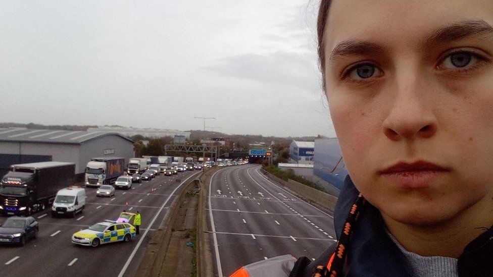 Just Stop Oil protester Louise standing on top a motorway gantry