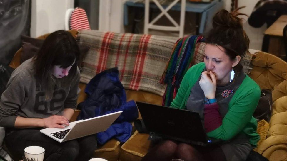 Two volunteers editing wikipedia at an event in Machynlleth sitting on the cafe sofa with laptops