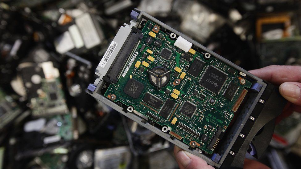 A worker holds a discarded hard drive from an old computer that will be stripped down to its parts in Berlin, Germany