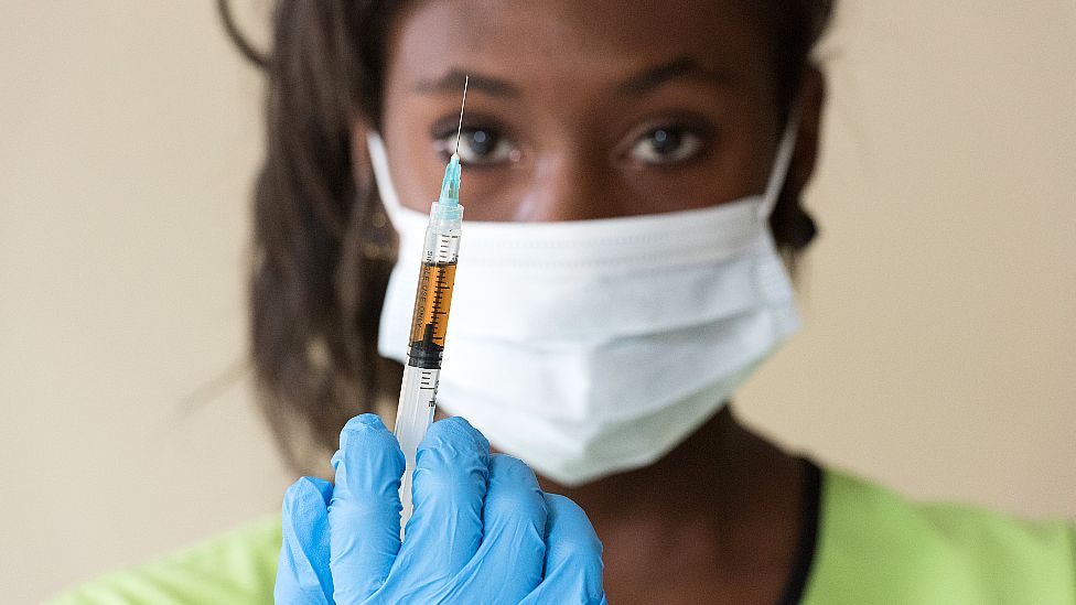 A generic photo of a masked nurse holding up a vaccine