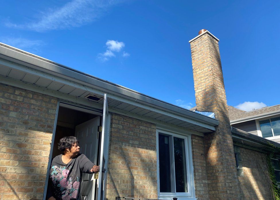 Рамона Бертон смотрит на свой отремонтированный дымоход и новые окна - работа стала возможной благодаря первой в своем роде программе репараций
