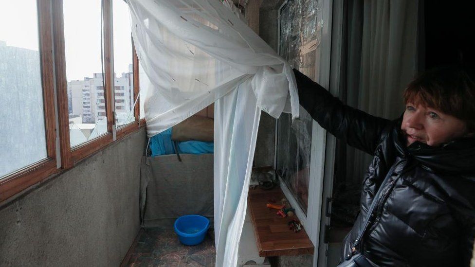 Một người phụ nữ cho thấy những ô cửa sổ bị vỡ trên ban công của mình sau một cuộc tấn công bằng tên lửa ở Kiev, ngày 09 tháng 3 năm 2023