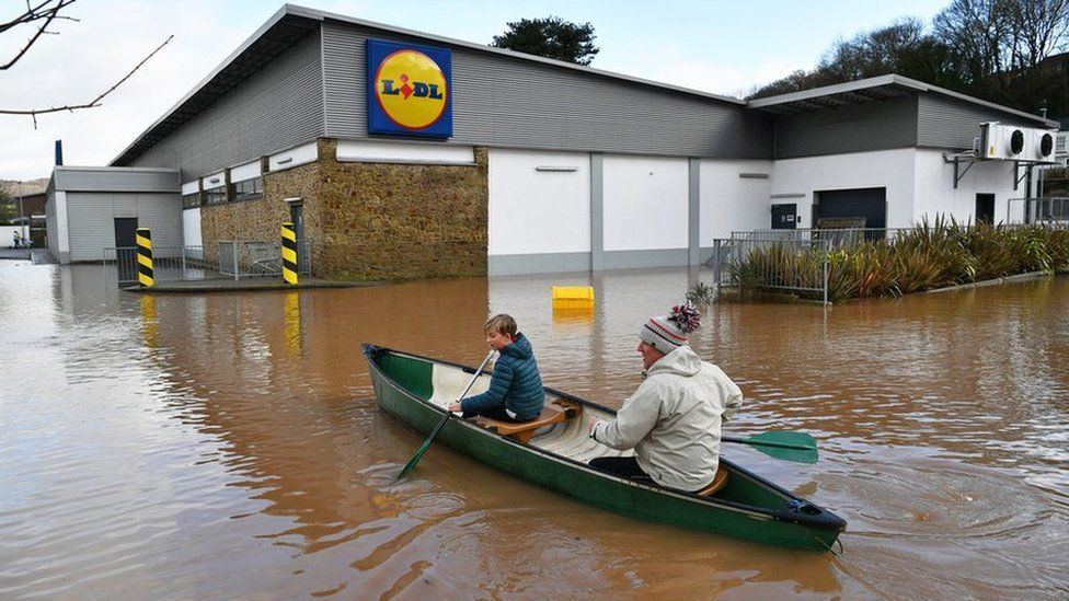 Two people in canoe rowing by a Lidl store in Monmouth