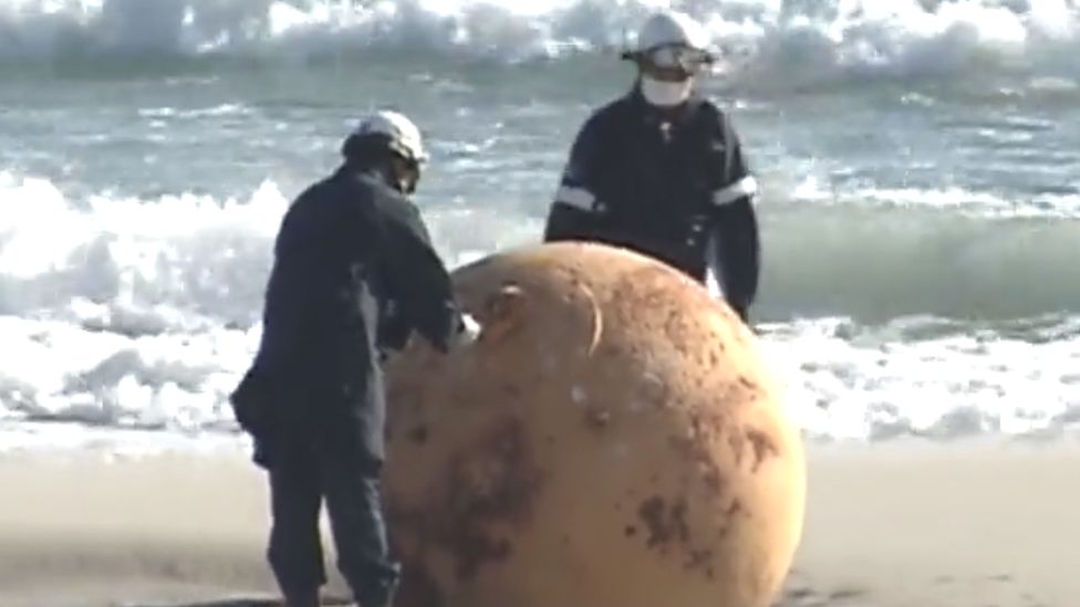 Two police officers examine the big metal boulder found on the beach in Hamamatsu