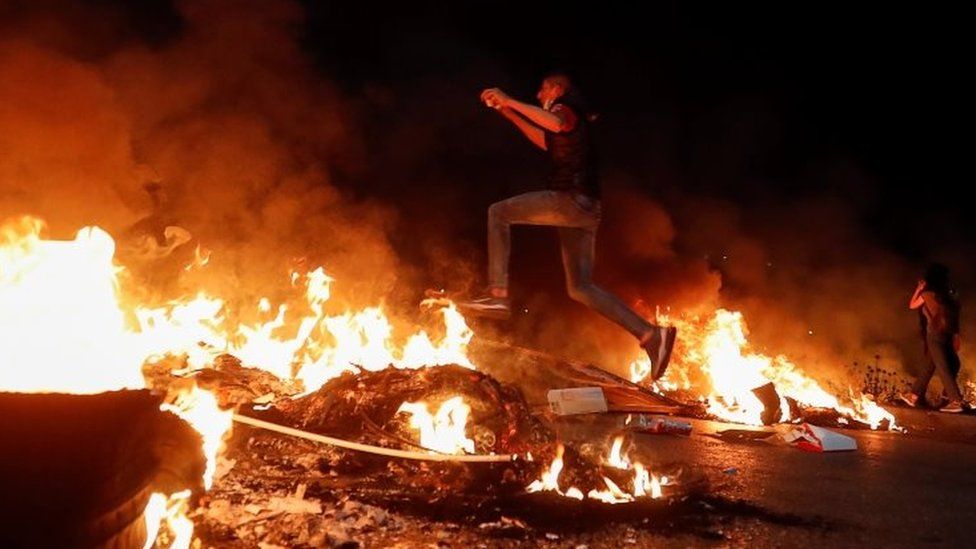 A Palestinian protester jumps over a burning barricade near the West Bank city of Ramallah. Photo: 9 May 2021