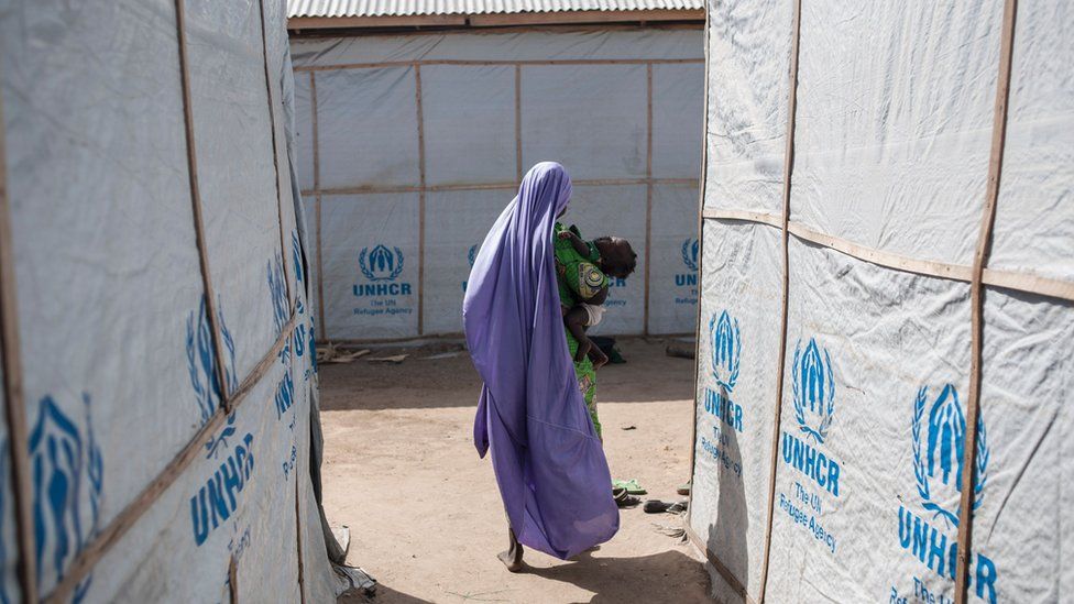 A woman carrying her baby walks through the temporary shelters provided by the Mission for the United Nations High Commissioner for Refugees (UNHCR) in one of the hosting communities in Maiduguri in northeastern Nigeria on December 7, 2016.