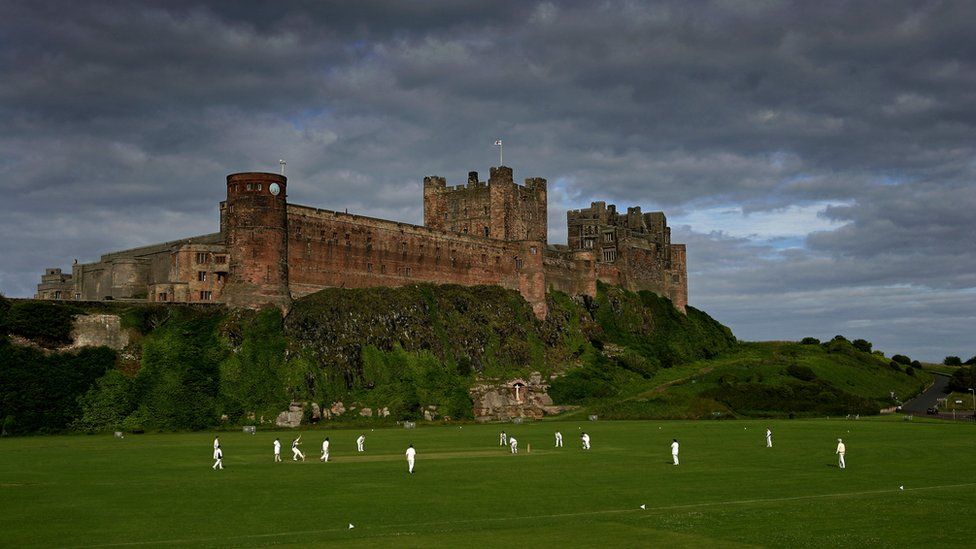 Cricketers play on pitch next to Bamburgh