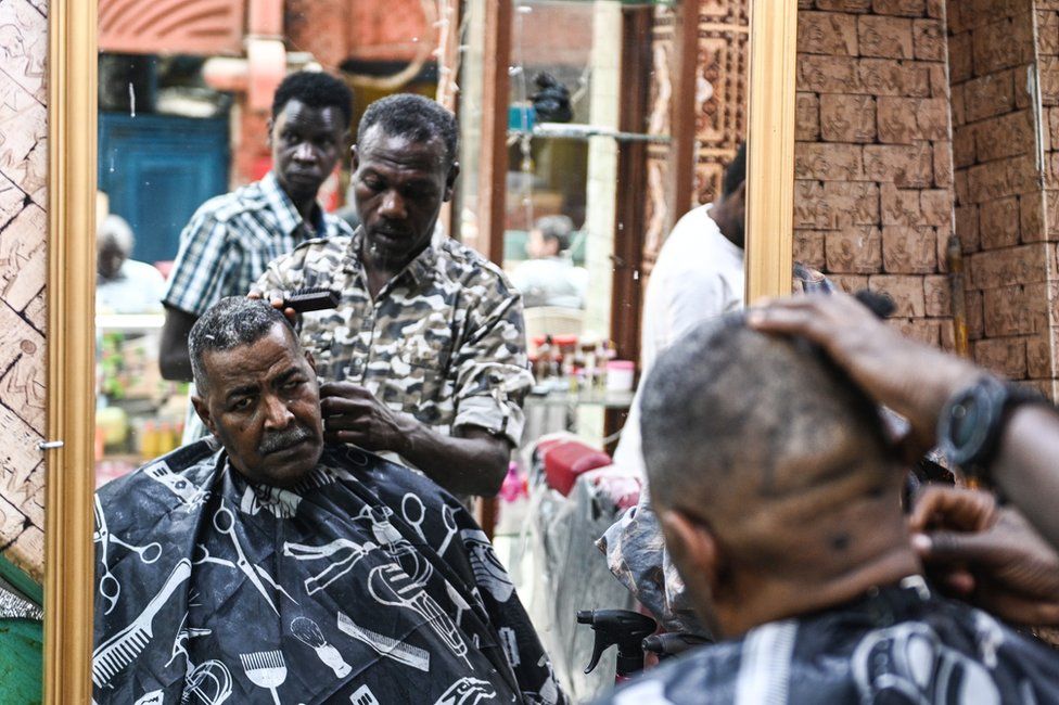 A Sudanese man has his hair cut in front of a mirror.