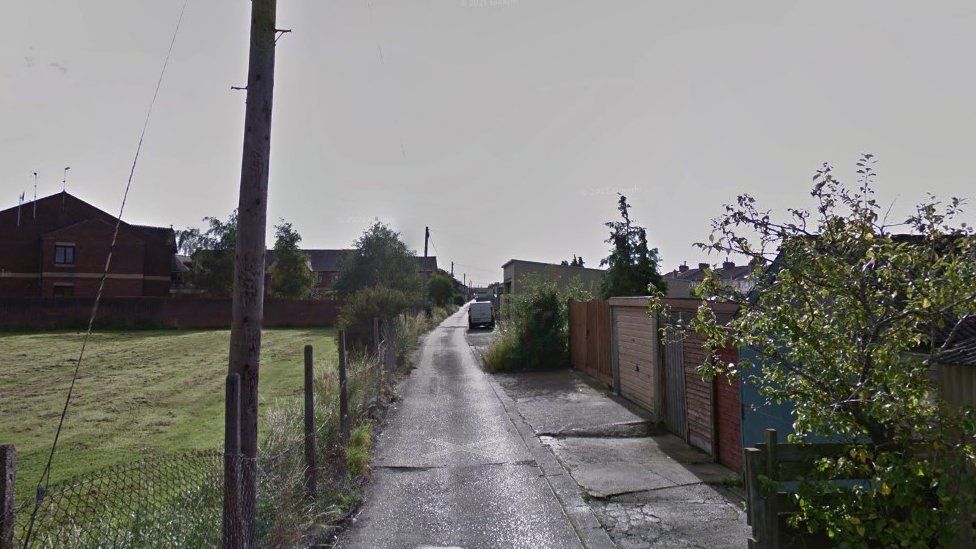 Google Maps image showing an alleyway off Ferndale Road in Swindon. There is a field to the left of the pathway which is fenced off by wire. To the right, shrubbery, fences and garages can be seen.