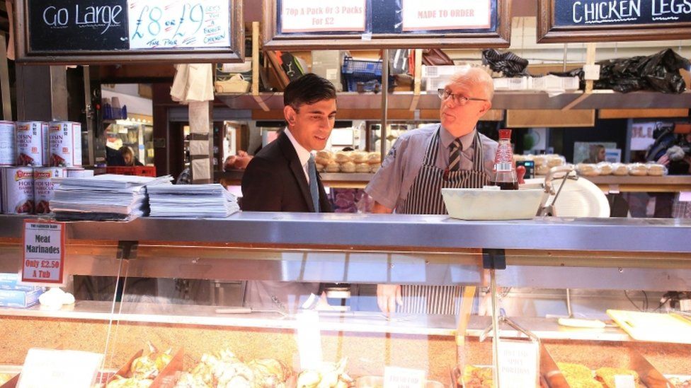 Chancellor of the Exchequer Rishi Sunak (left) speaks to a butcher during a visit to Bury Market