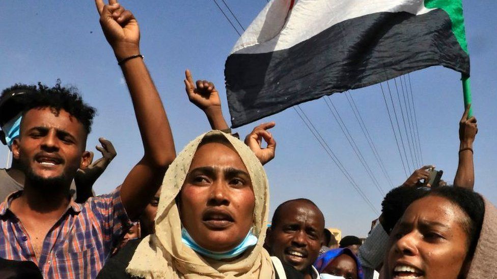 Sudanese protesters flash victory signs and lift natioanl flags as they demonstrate on 60th Street in the capital Khartoum, to denounce overnight detentions by the army of government members, on October 25, 2021.