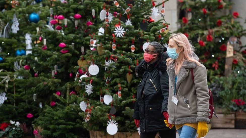 Two people wearing face masks by Christmas trees
