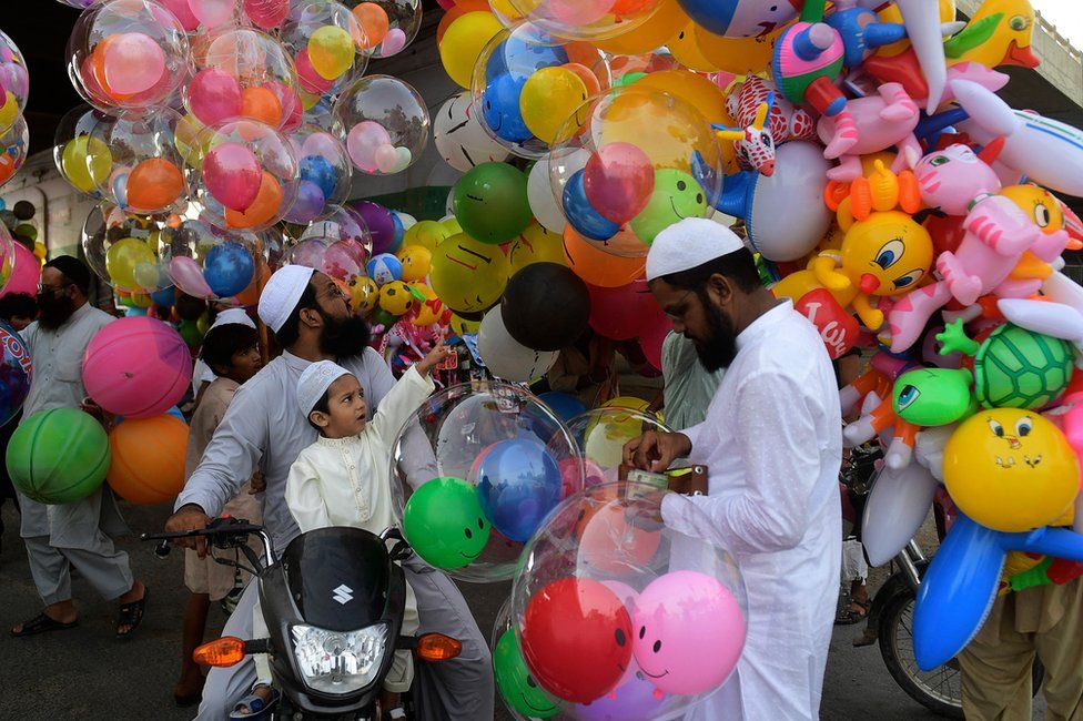 A child points to a balloon while sitting on a motorbike with an adult