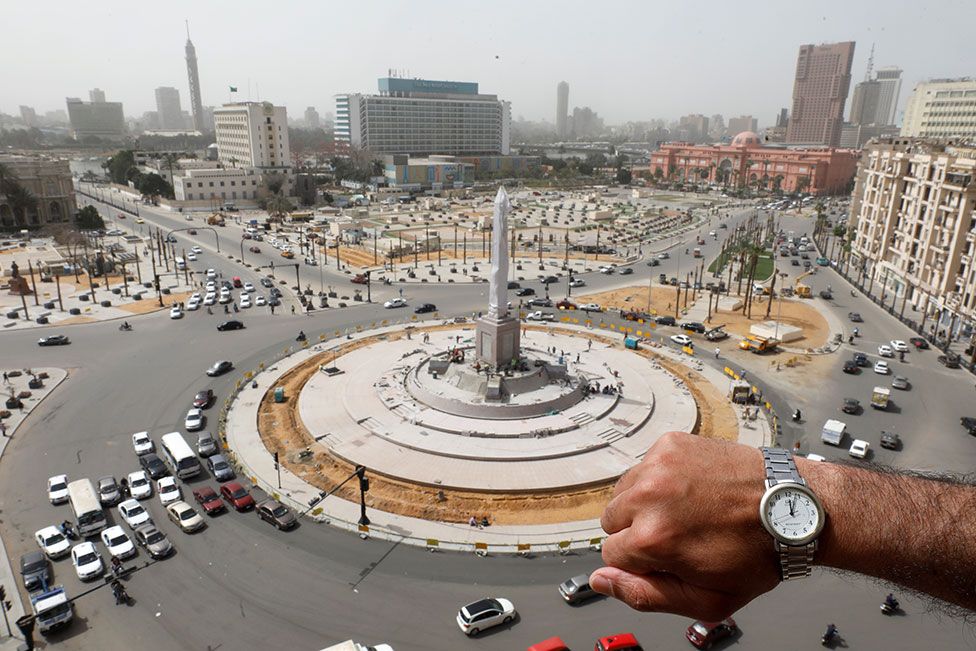 A wristwatch showing noon with Tahrir Square, Cairo, in the background