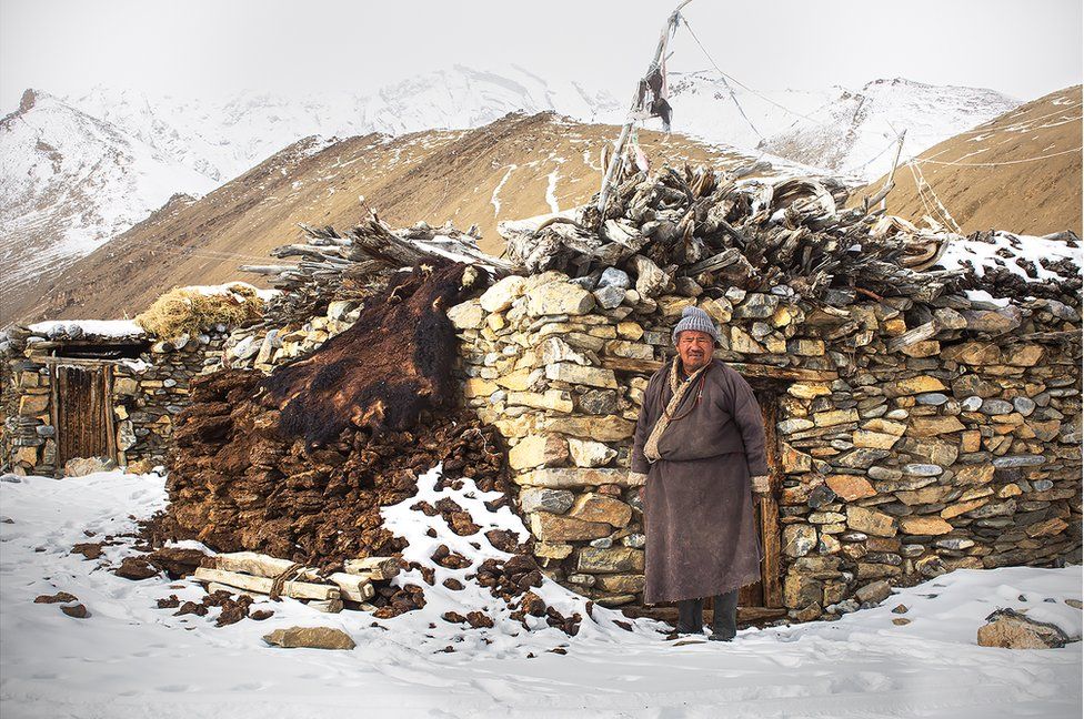 A herder stands in front of his stone house