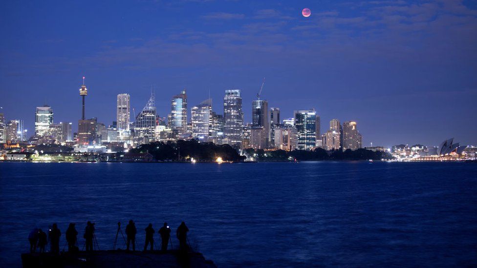 The moon is seen turning red over the Sydney skyline during a total lunar eclipse on July 28, 2018 in Sydney, Australia.