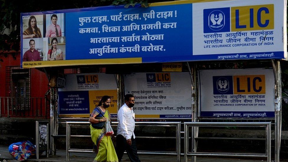 People walk past a bus shelter showing advertisement of country's largest insurer public, Life Insurance Corporation of India (LIC) in Mumbai
