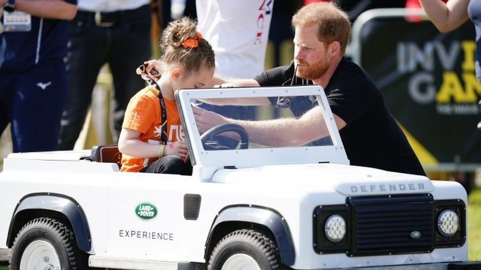 The Duke of Sussex gives a medal to a child driving a toy Land Rover at the Jaguar Land Rover Driving Challenge during the Invictus Games