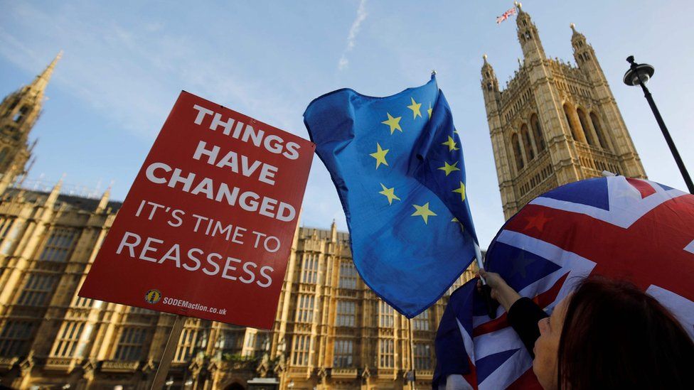 An anti-Brexit placard outside Parliament demands a reassessment of the options, while EU and Union Jacks are waved