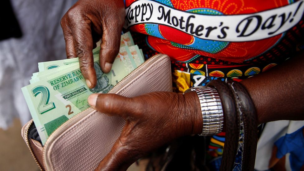 A woman poses with Zimbabwe"s new two dollar banknotes as customers queue outside a bank in Harare, Zimbabwe,