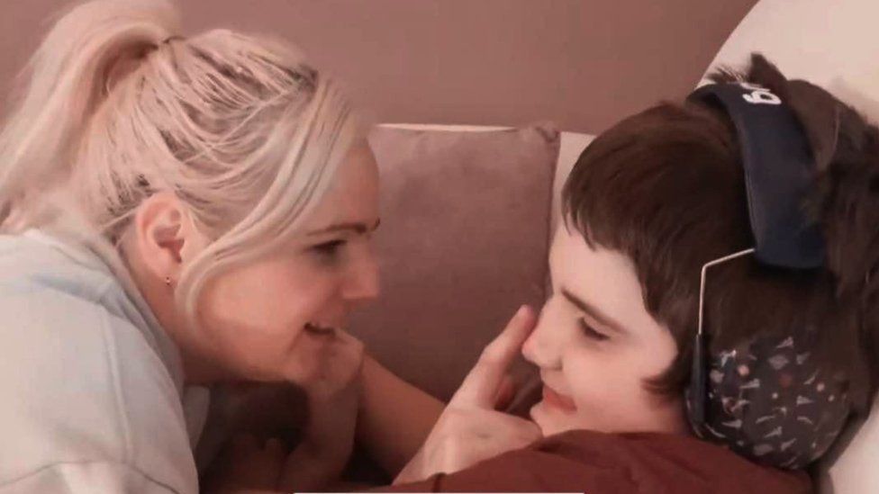 Charlotte looks at her son with a smile Tobie while touching his nose with her finger. Tobie is smiling, he is wearing a set of ear defenders