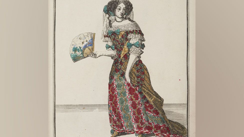 A drawing of a late 17th Century woman with curling black hair puffed out on either side and a lace veil flowing behind, and a yellow, red and green dress with white lace low cut collar and sleeves, green bows while carrying a fan