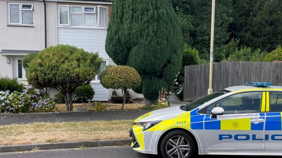 Police car outside terrace house with tree and bushes in background