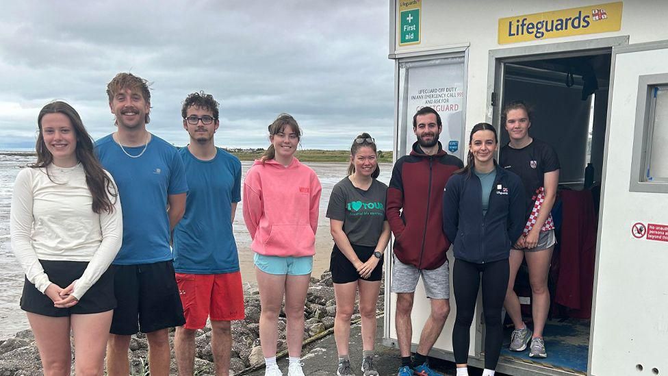 Eight lifeguards stand outside hut on Wirral coastline