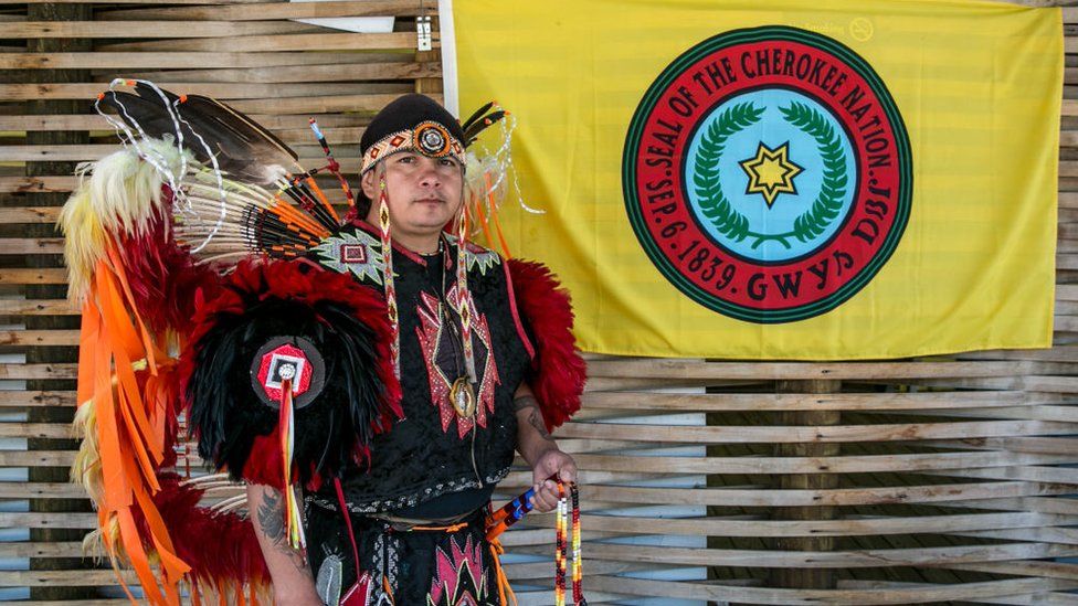A native American poses by the Cherokee Nation flag